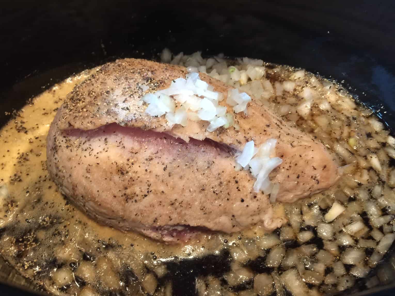 Picture of browned pork roast with onions and rootbeer in a slow cooker.