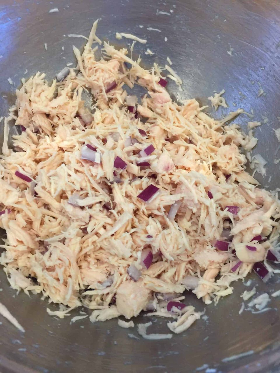 Shredded chicken and red onion in a bowl for the Best Chicken Salad Ever.