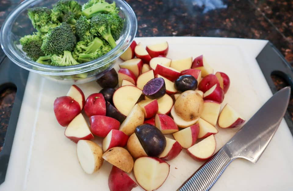 Baby potatoes and broccoli cut into bite sized pieces on a cutting board, with a knife.