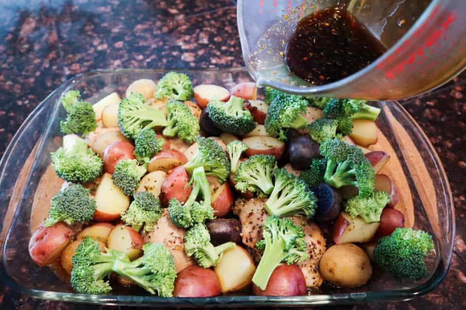 The rest of the honey garlic sauce being poured over broccoli, potatoes and chicken in the baking dish.