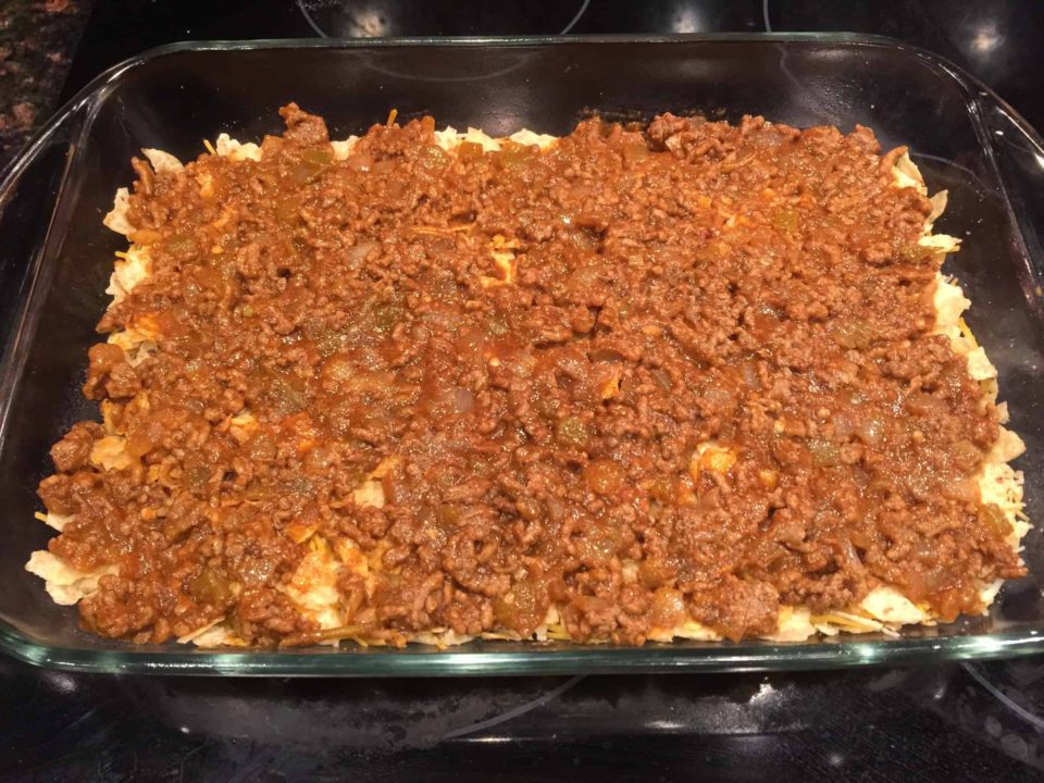 Middle meat layer over bottom broken chip layer in baking dish for Oven Baked Taco Casserole.