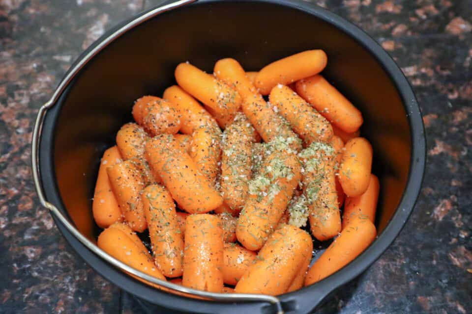 Carrots in a pot with dill, minced garlic, kosher salt & ground pepper on top.