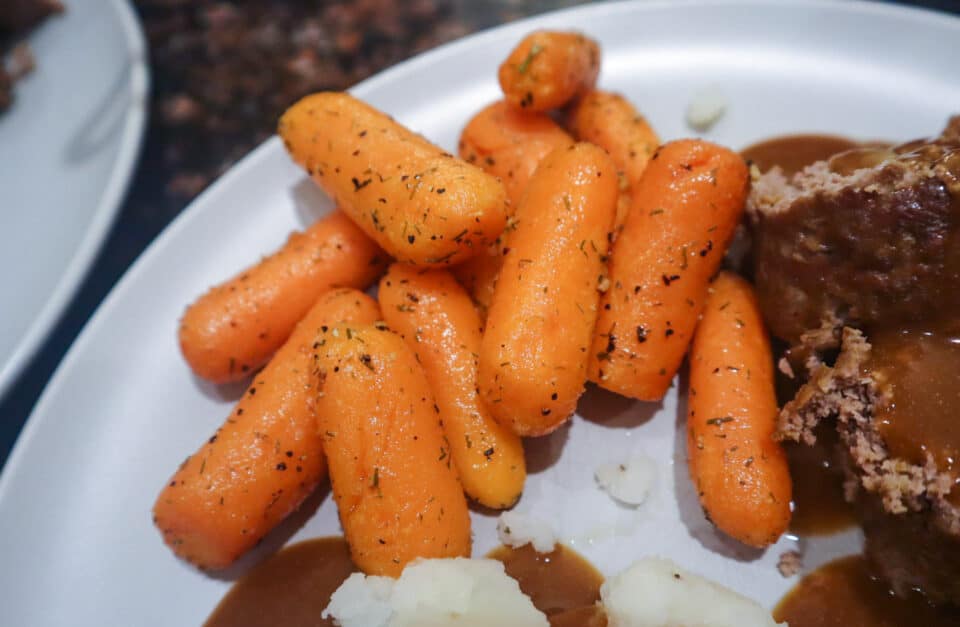 Finished Air Fryer Roasted Baby Carrots on a plate alongside meatloaf and mashed potatoes.