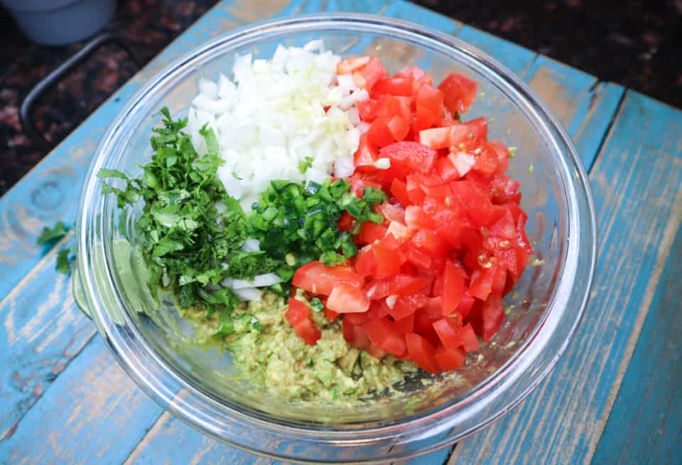 Tomatoes, onions, jalapenos and cilantro being added to avocado mixture.