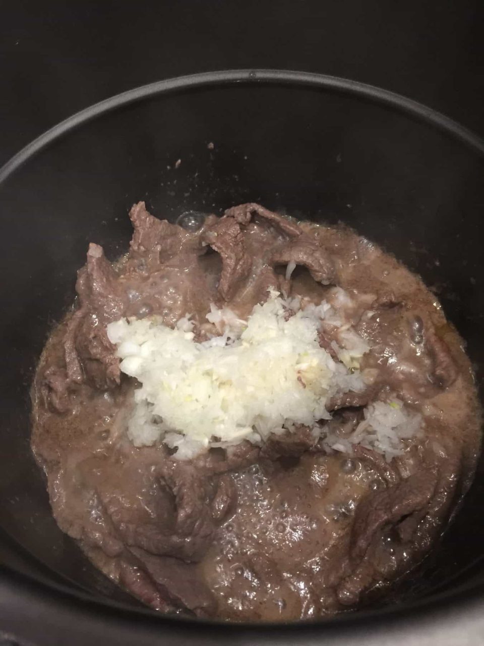 Raw onions and garlic added to beef slices in instant pot for Instant Pot Beef with Broccoli