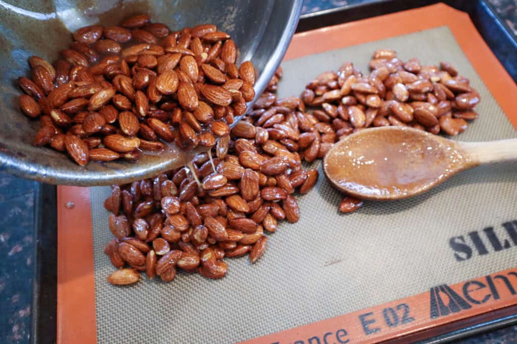 Spreading the coated almonds onto the prepared baking sheet prior to roasting.