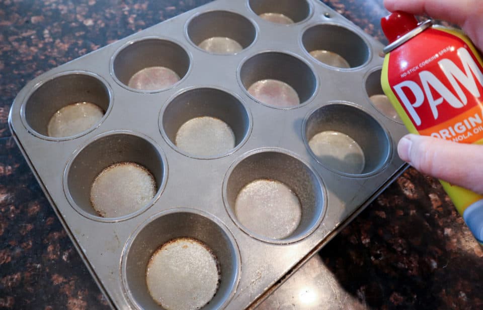 Muffin tin being sprayed with cooking spray
