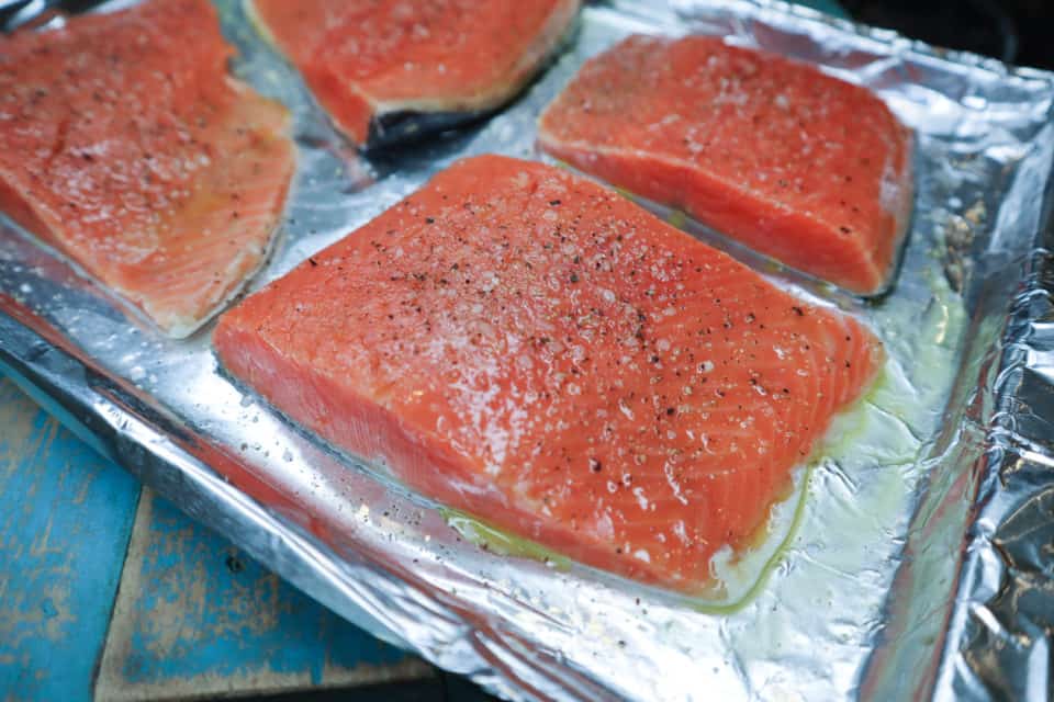 Picture of salmon fillets up close seasoned with kosher salt and pepper prior to baking. 