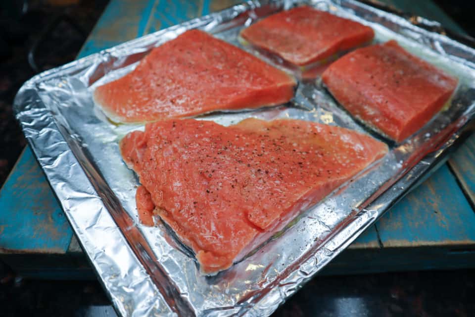 Salmon fillets om a baking sheet seasoned with kosher salt & pepper before baking.