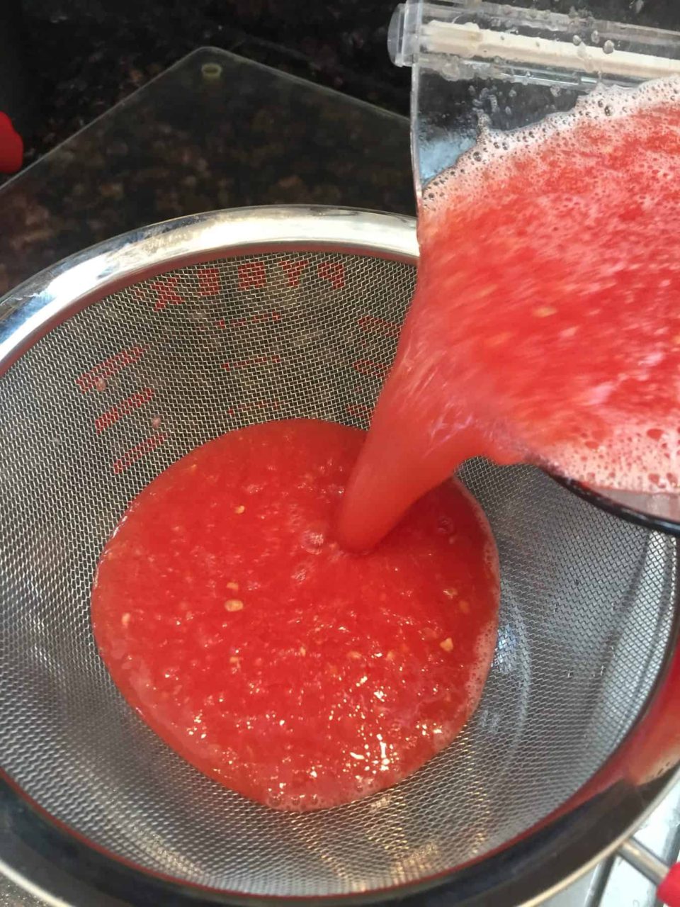 Picture of watermelon liquid being strained in a mesh strainer for Watermelon Lime Sorbet
