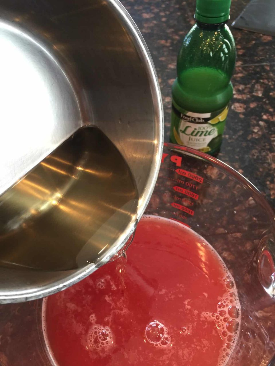 Picture of simple syrup being added to watermelon juice for Watermelon Lime Sorbet.  Lime juice pictured in the background