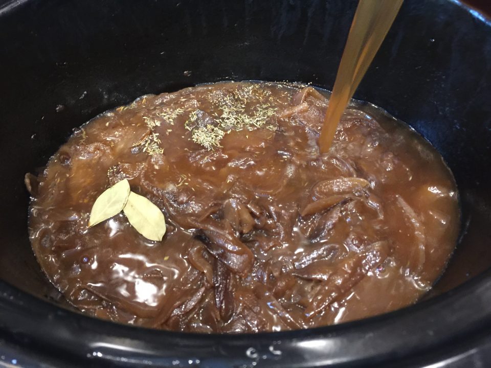 Pouring broth over the caramelized onions and into the slow cooker for Crock Pot French Onion Soup.