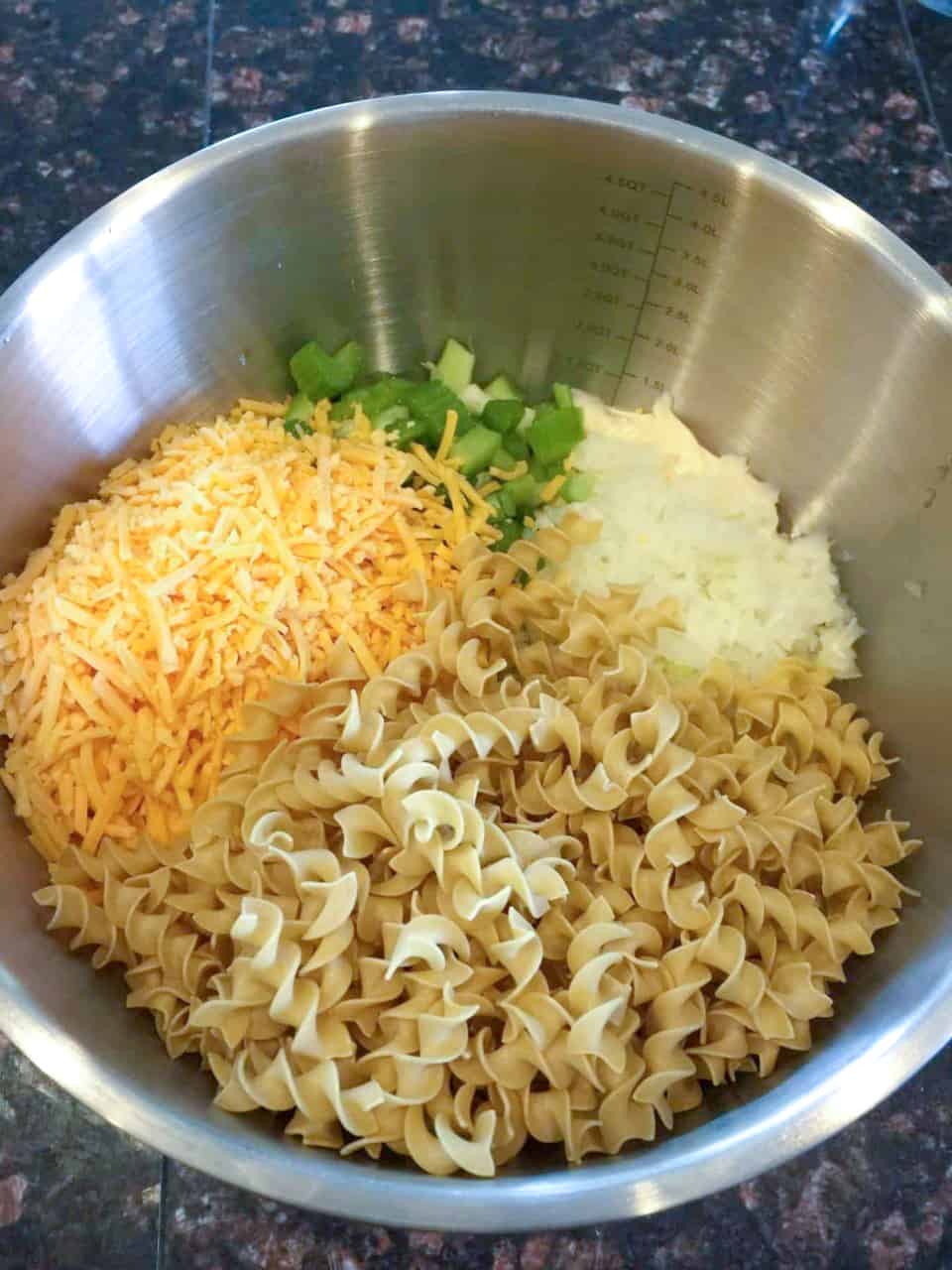 Ingredients for Turkey Noodle Casserole in a bowl. Pictured - egg noodles, shredded cheese, onion and celery.