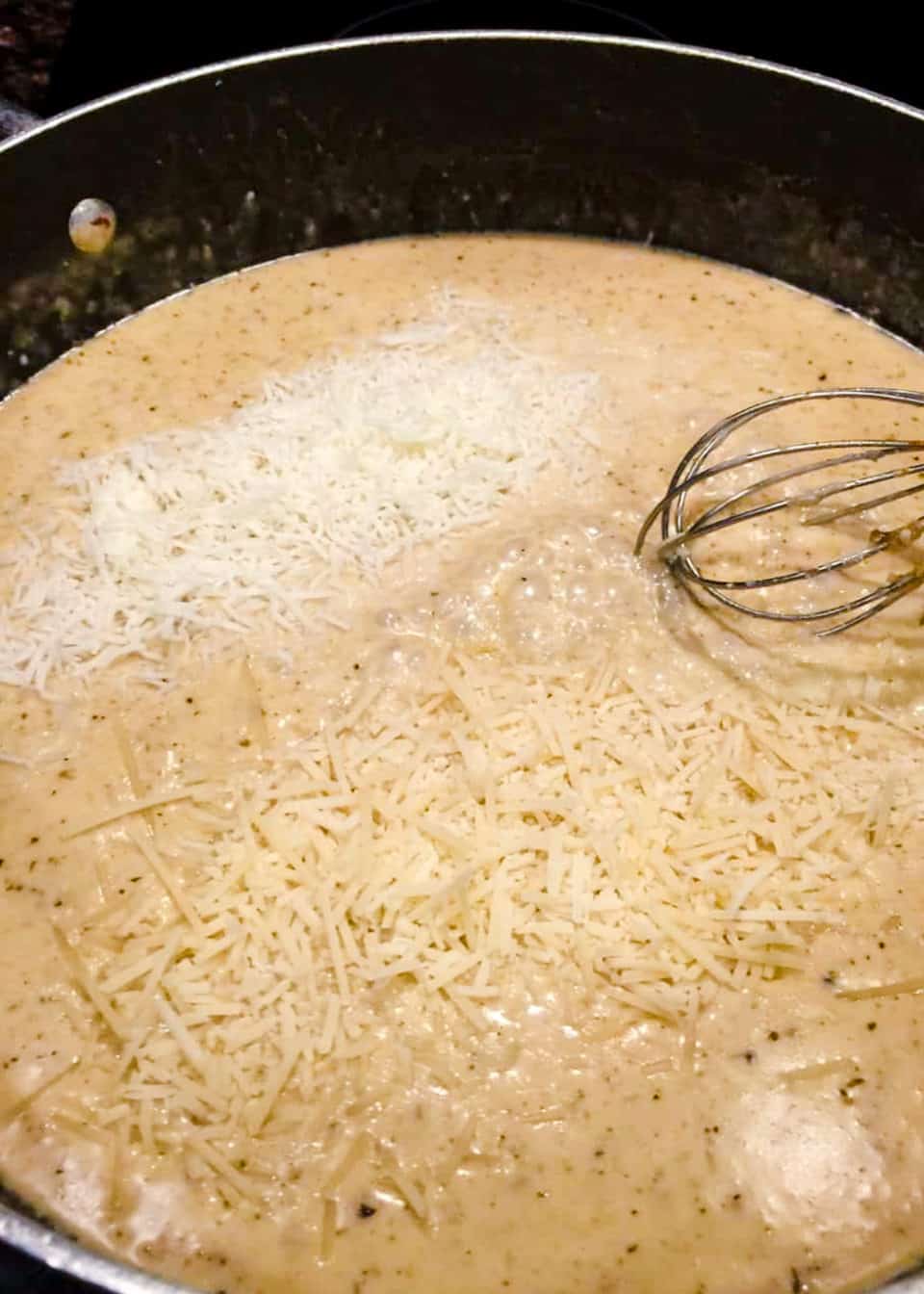 Adding cheese to the skillet with a whisk.