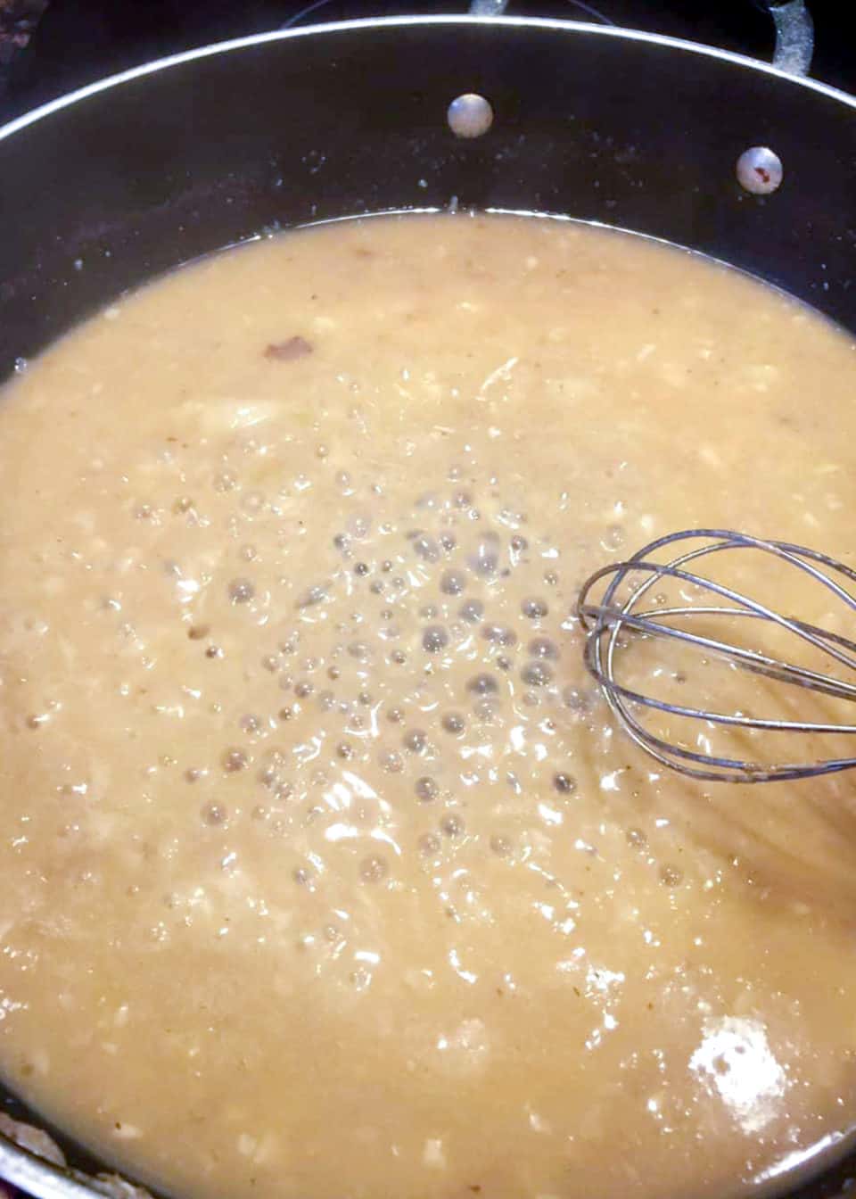 Bubbling sauce and a whisk in a skillet.