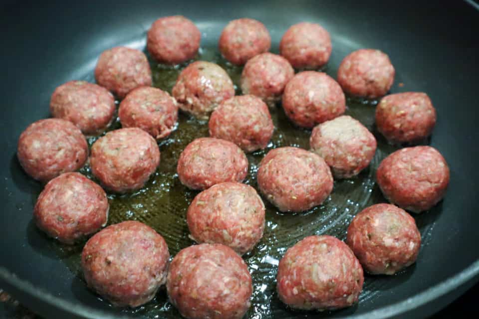Raw meatballs in a skillet getting fried up for Creamy Orzo with Meatballs and Peas.