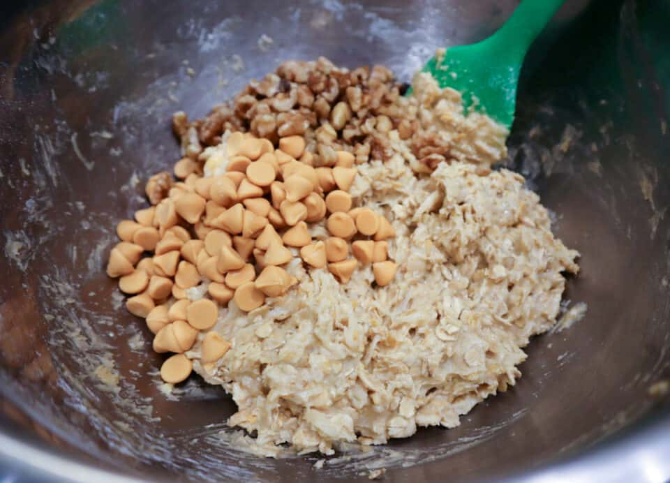 Stirring nuts and butterscotch chips into the batter with a spatula.