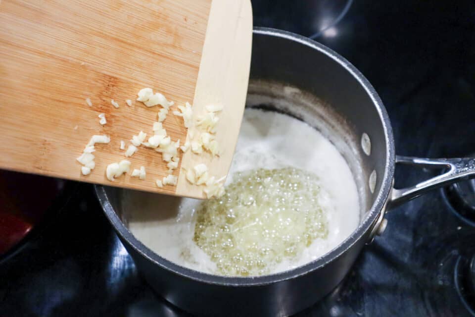 Adding chopped garlic to melted butter in a saucepan.