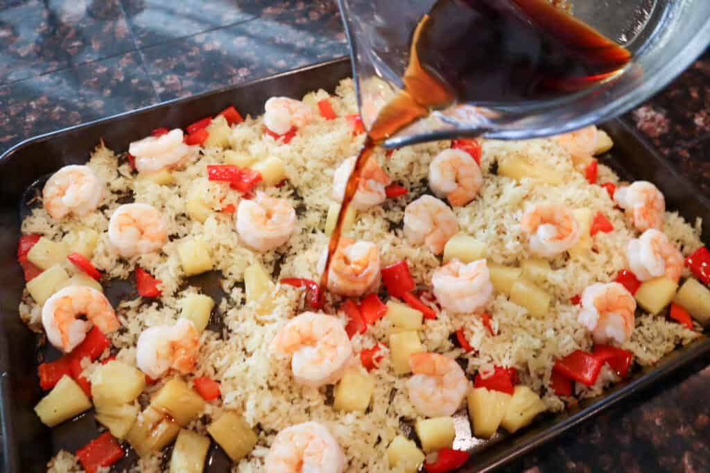 Adding the island sauce to the finished Pineapple Shrimp and Rice Bake on the sheet pan.