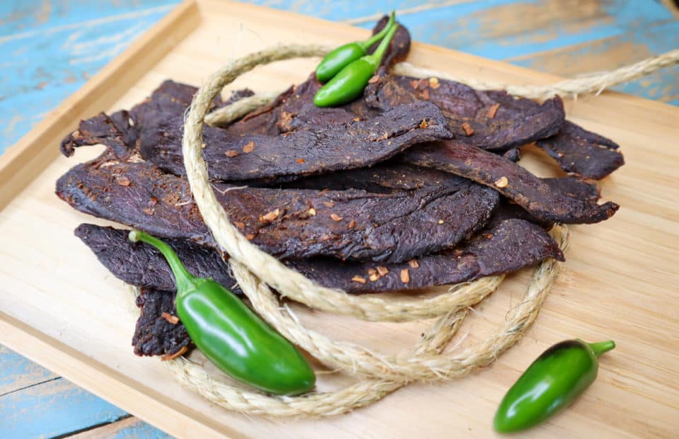 Finished Sweet & Spicy Beef Jerky on a board with Jalapenos.