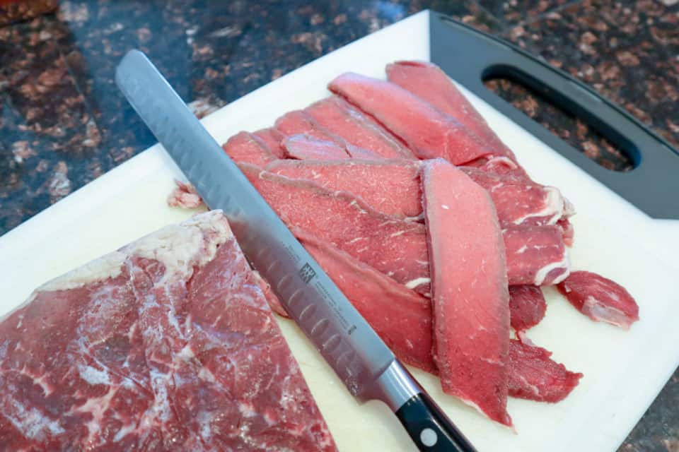 Meat being cut for Sweet & Spicy Beef Jerky on a cutting board with a knife.