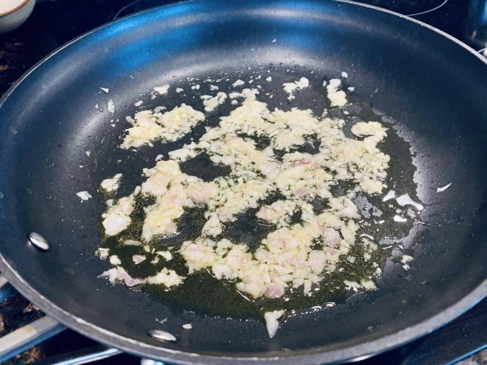 Oil, garlic and shallots being sauteed in a skillet for Homemade Mushroom Ravioli filling.