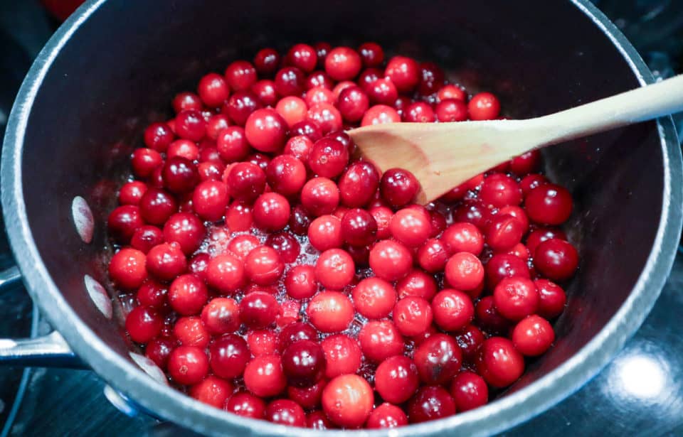 Fresh cranberries in a saucepan with simple syrup and a wooden spoon.