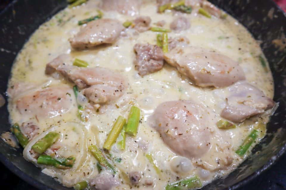Picture of asparagus, chicken thighs and onions mixed into cream sauce in the skillet