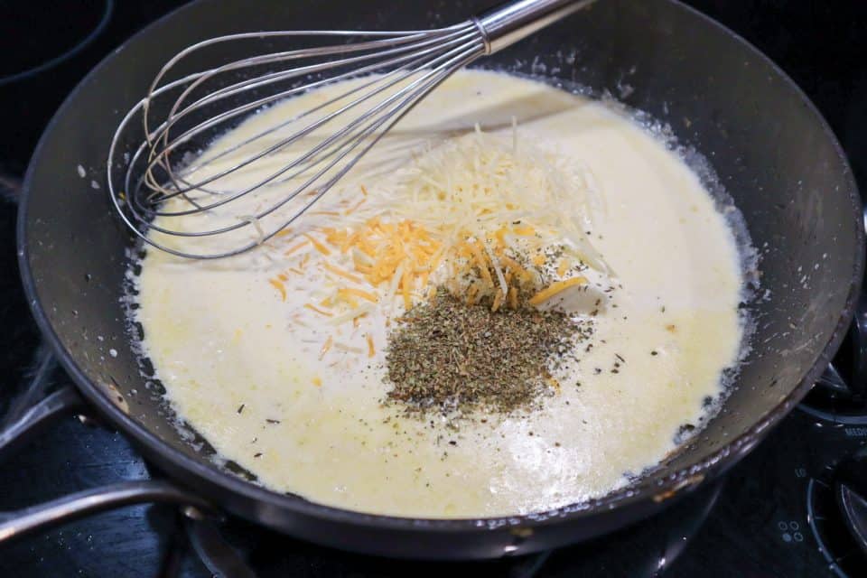 Picture of cheese and seasonings being added to cream sauce in a skillet