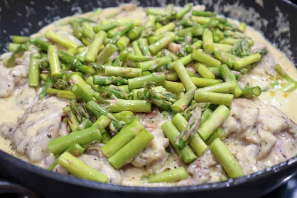 Picture of asparagus being added to chicken thighs and onions in cream sauce in the skillet