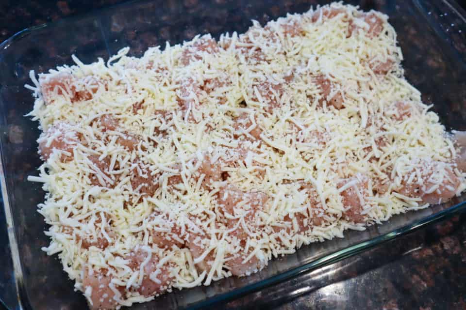 Picture of raw chicken covered in a layer of shredded mozzarella cheese in a baking pan