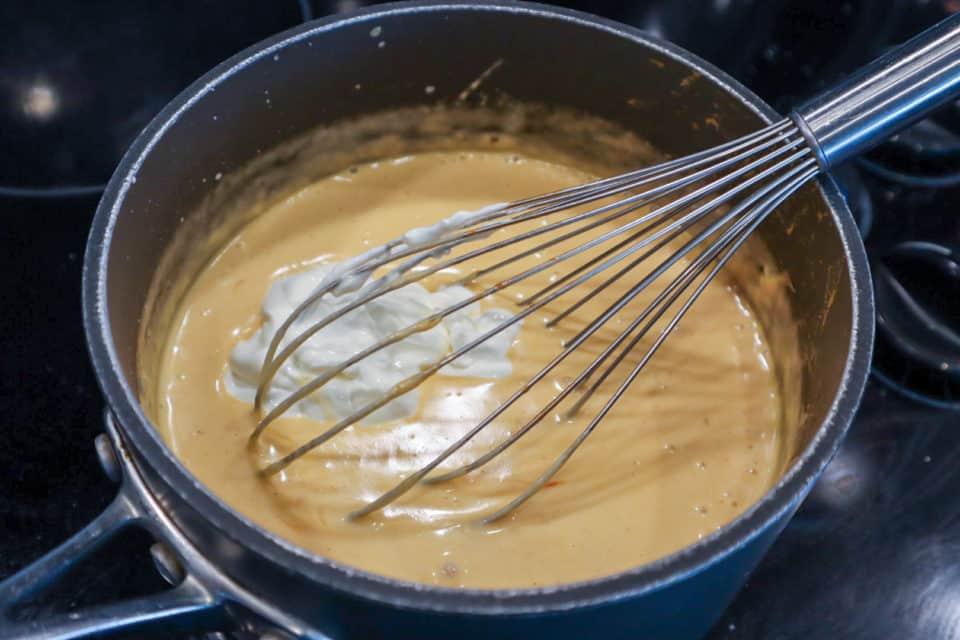 Picture of sour cream being whisked into cheese sauce mixture for Buffalo Chicken Mac & Cheese