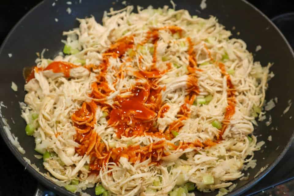 Picture of shredded chicken, onions, celery and hot sauce in a skillet for Buffalo Chicken Mac & Cheese
