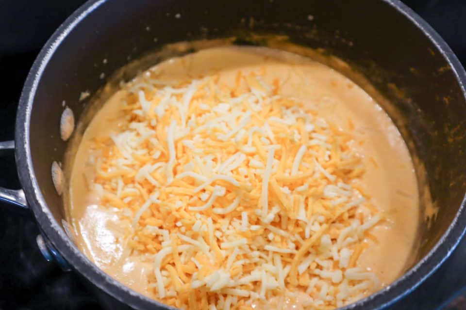 Picture of shredded cheese being added to mixture for Buffalo Chicken Mac & Cheese