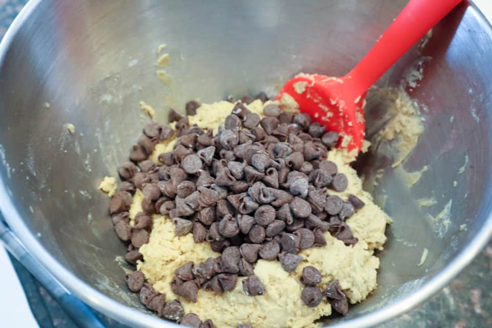 Picture of chocolate chips being folded into the dough with a spatula for Fudgy Salted Cookie Bars.