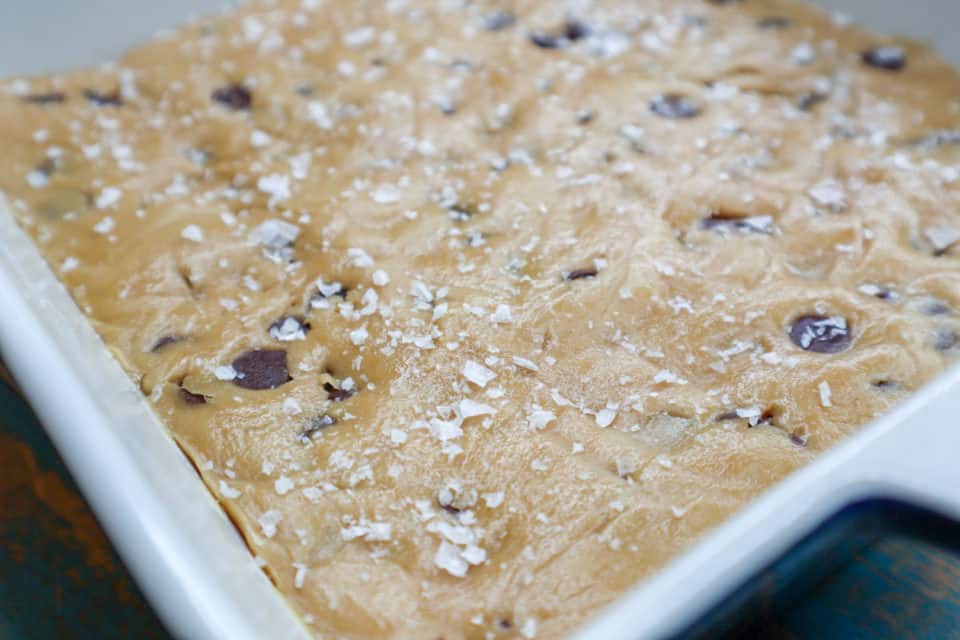 Picture of dough spread out in a baking pan and sprinkled with flaky sea salt for Fudgy Salted Cookie Bars.