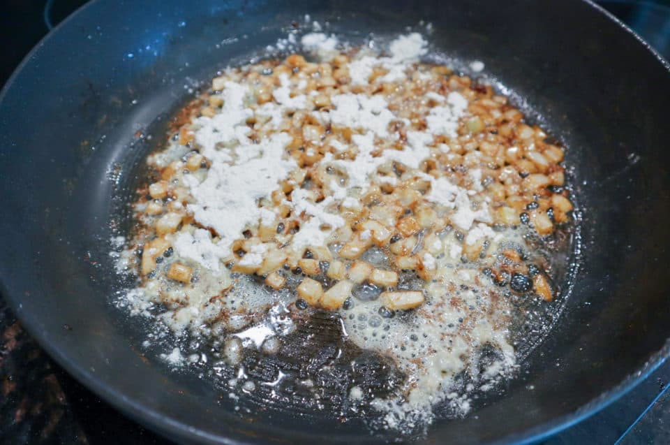 Picture of cooked onions sprinkled with flour in a skillet for Easy Pork Chops with Pan Sauce.
