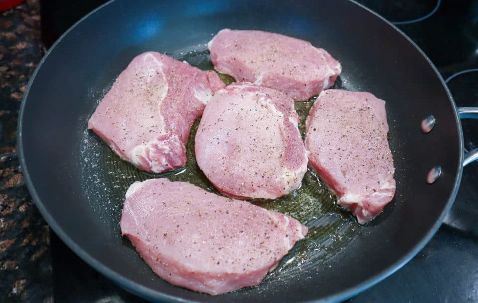 Picture of pre cooked pork chops seasoned with salt and pepper in a skillet with oil for Easy Pork Chops with Pan Sauce.