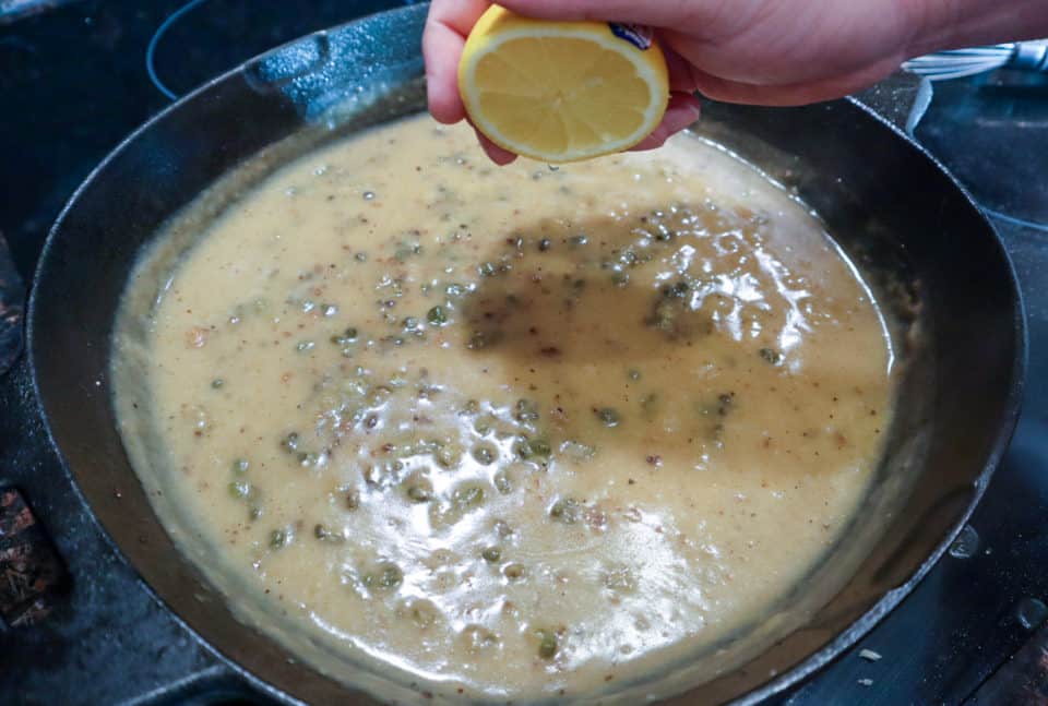 Half of a fresh lemon being squeezed into the pan sauce in the cast iron pan for the Pork Scallopini with Lemon Caper Sauce.