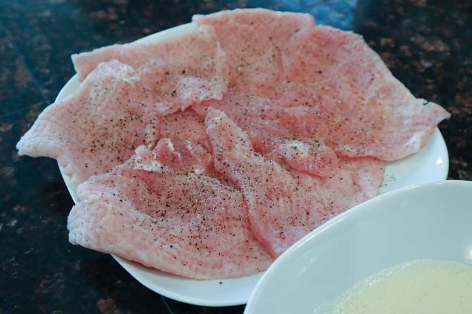 Salt and peppered thin pork chops prior to breading for Pork Scallopini with Lemon Caper Sauce.