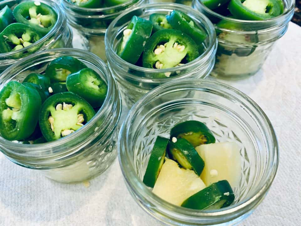 Picture of sliced jalapenos and pineapple in small jars for Pineapple Cowboy Candy.