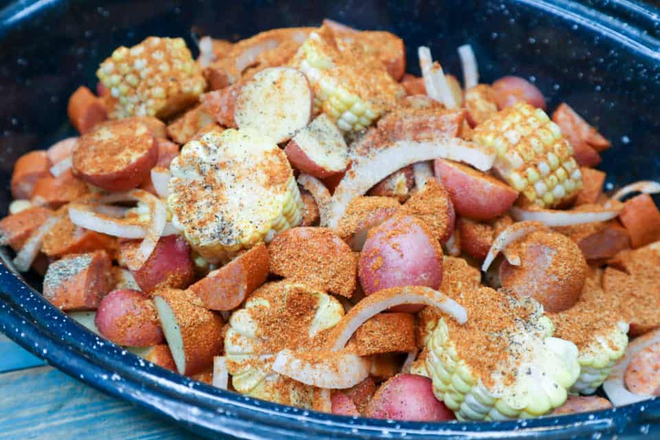 Corn, sausage, onion and potatoes in a roaster pan sprinkled with seasonings for Sunday "Shrimp Boil" Bake