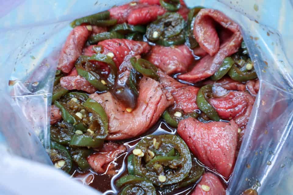 Picture of beef marinating in jalapenos and marinade in a zip top bag for Spicy Dr. Pepper Beef Jerky.