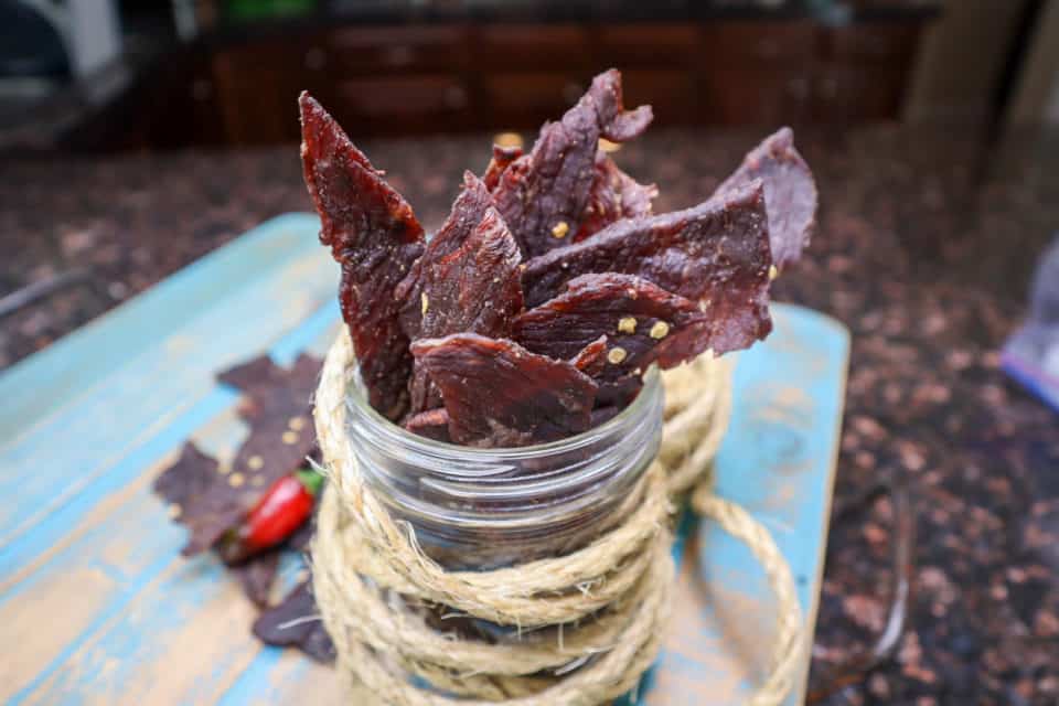 Picture of finished Spicy Dr. Pepper Beef Jerky in a jar and on a blue board.