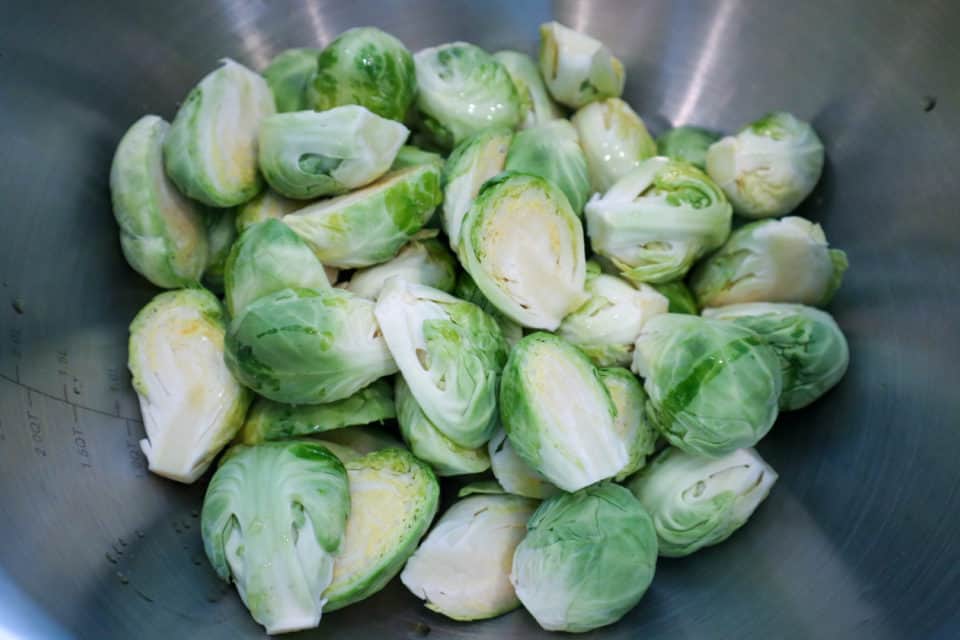 Picture of raw cleaned Brussels sprouts cut in half in a bowl.