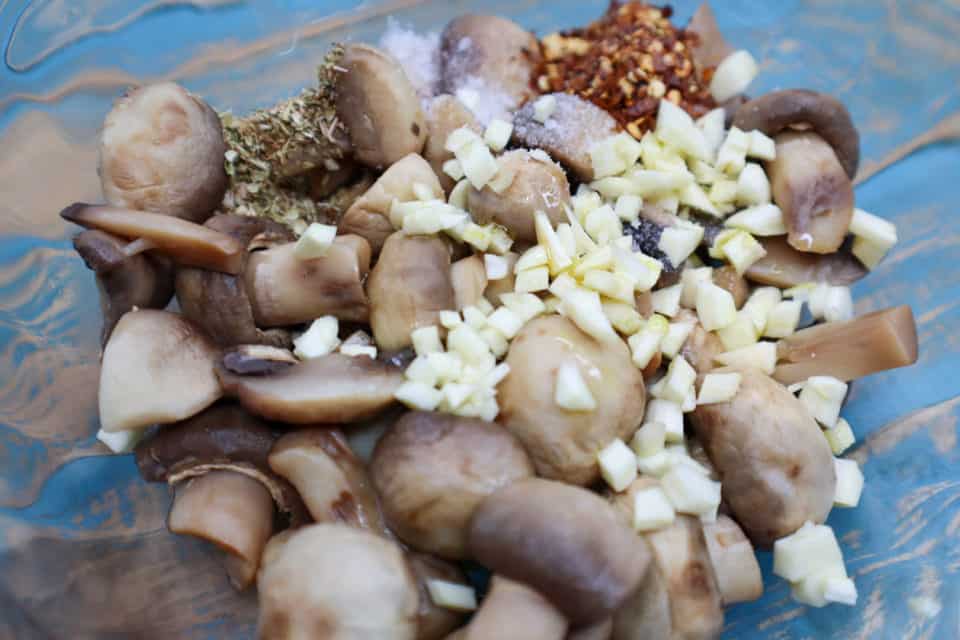 Picture of mushrooms, garlic, spices and oil in a bowl for Easy Italian Pickled Mushrooms.