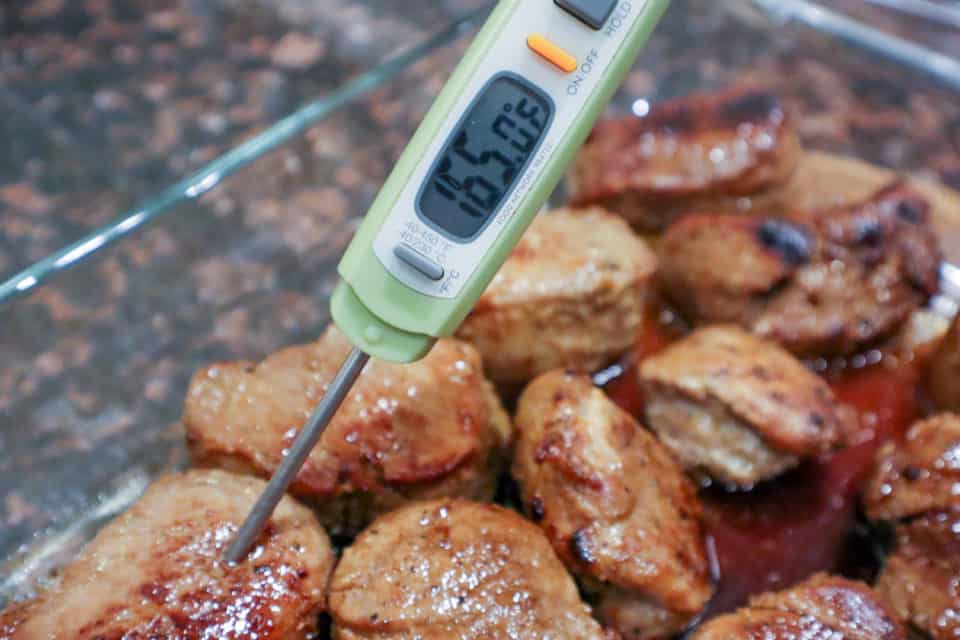 Instant read thermometer showing 165 degrees F inserted in a pork medallion.