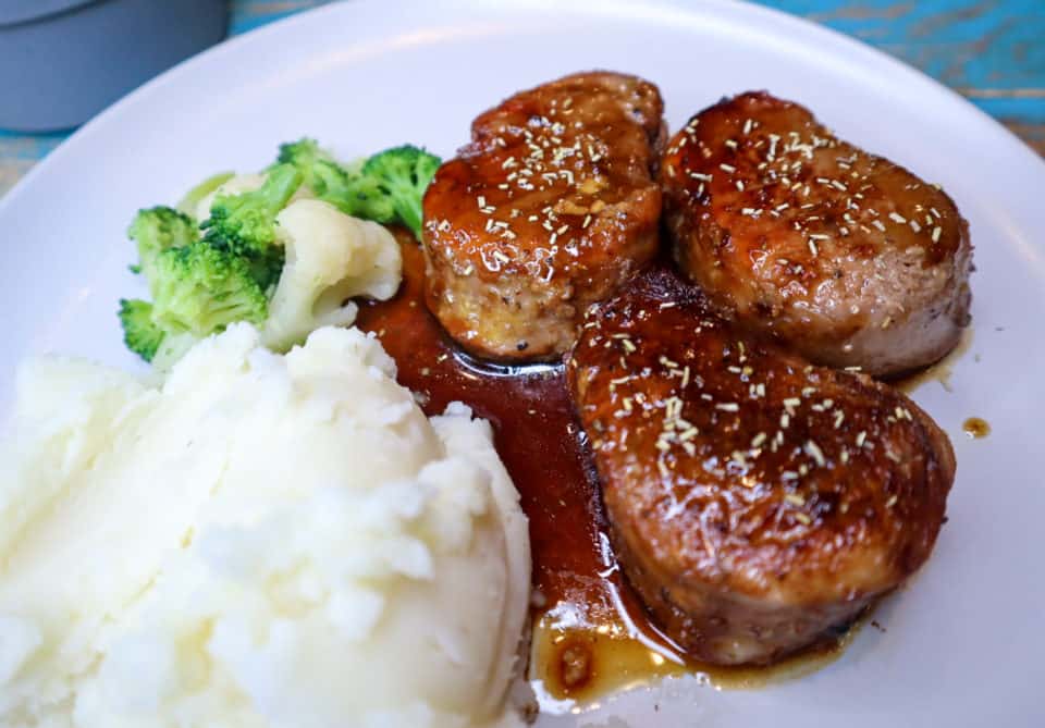 Finished Pork Medallions with Balsamic Honey Sauce on a plate with Mashed potatoes and broccoli.