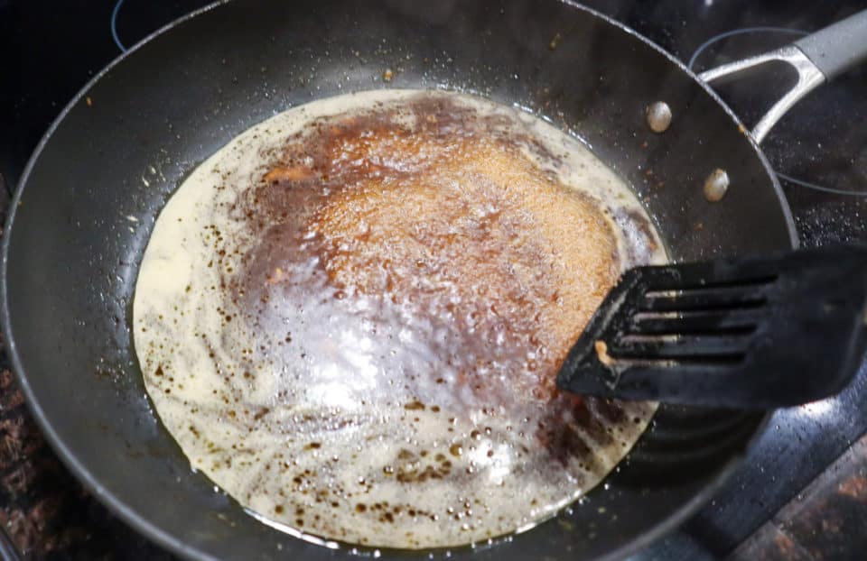 Skillet being deglaxed with spatula on the right.