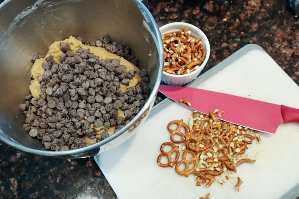 Pretzels and a knife on a cutting board in whole and chopped states. Bowl with chocolate chips.